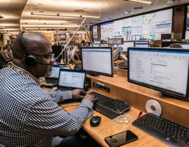 A employees speaking in front of several computer screens.